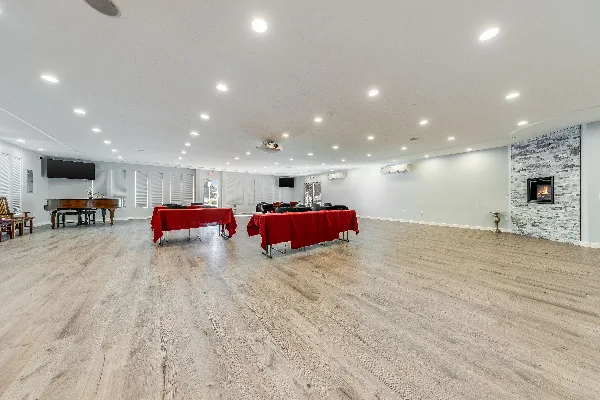 Interior view of a spacious event hall with light wood flooring, a grand piano, and a stone fireplace.