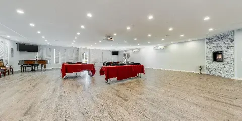 Interior view of a spacious event hall with light wood flooring, a grand piano, and a stone fireplace.