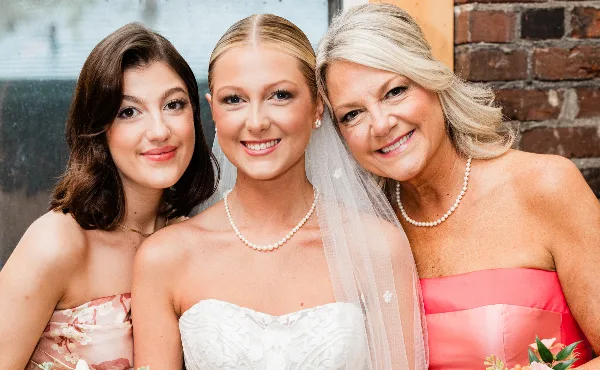A bride in a white dress and veil posing with two women in formal dresses.