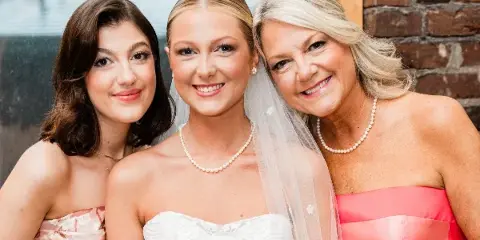 A bride in a white dress and veil posing with two women in formal dresses.