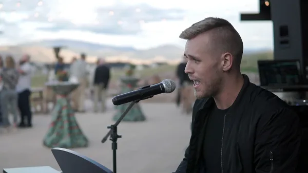 A DJ performing at an outdoor wedding reception with guests in the background.