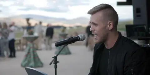 A DJ performing at an outdoor wedding reception with guests in the background.