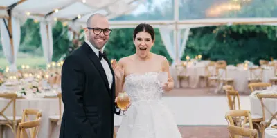 A bride and groom standing in a decorated wedding tent with string lights and set tables.