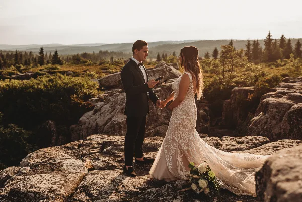 A bride and groom holding hands on a rocky mountain overlook during a wedding session.