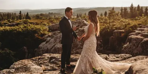 A bride and groom holding hands on a rocky mountain overlook during a wedding session.