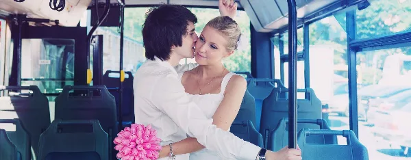 A bride and groom embracing inside a shuttle bus with a pink bouquet.