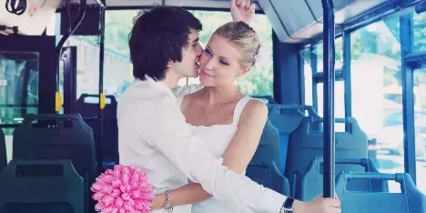 A bride and groom embracing inside a shuttle bus with a pink bouquet.