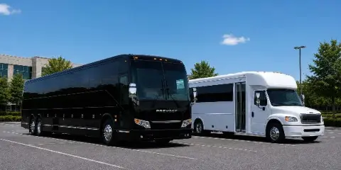 A black Prevost charter bus and a white minibus parked side-by-side in a parking lot.