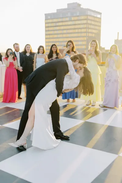 A bride and groom dancing on a checkered dance floor at a rooftop wedding reception with guests in the background.