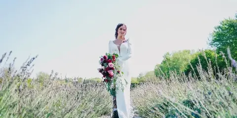 A bride in a white dress holding a bouquet of flowers in a lavender field.