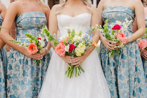 Bride and bridesmaids in blue floral dresses holding colorful wedding bouquets