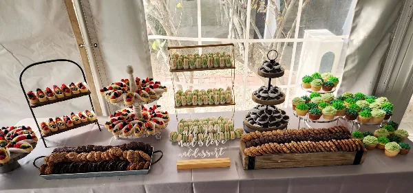 A wedding dessert table display featuring macarons, decorated cupcakes, cookies, and fruit tarts arranged on tiered stands and trays.