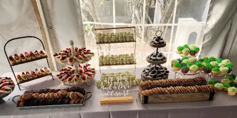 A wedding dessert table display featuring macarons, decorated cupcakes, cookies, and fruit tarts arranged on tiered stands and trays.