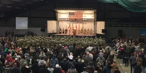 Large indoor event hall with a stage, American flag, and seated audience at a formal gathering.