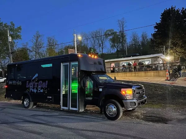 A black party bus with 'Let's Go! Party Bus' branding parked on a street at dusk.