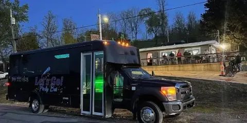 A black party bus with 'Let's Go! Party Bus' branding parked on a street at dusk.