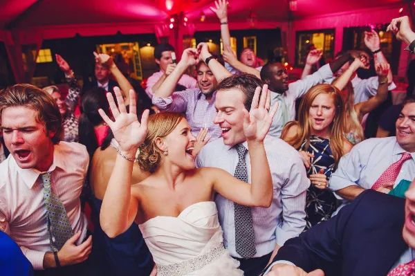 A bride and groom dancing joyfully with their guests at a wedding reception.