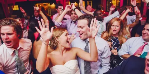 A bride and groom dancing joyfully with their guests at a wedding reception.