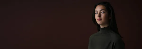 Cinematic portrait of a woman with dark hair wearing a dark turtleneck against a dark background.