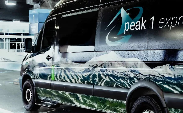 Peak 1 Express shuttle van parked at an airport terminal with mountain graphics on the side