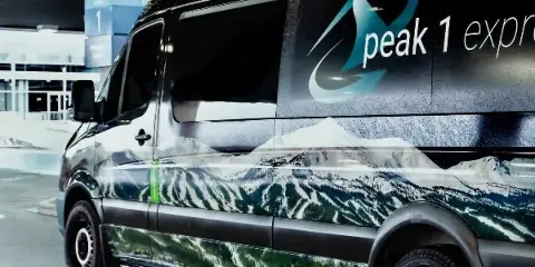 Peak 1 Express shuttle van parked at an airport terminal with mountain graphics on the side