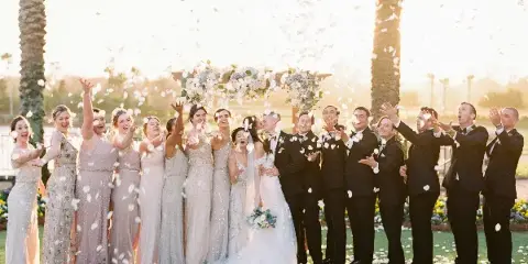 A wedding party including the bride, groom, and wedding party celebrating with flower petals outdoors.