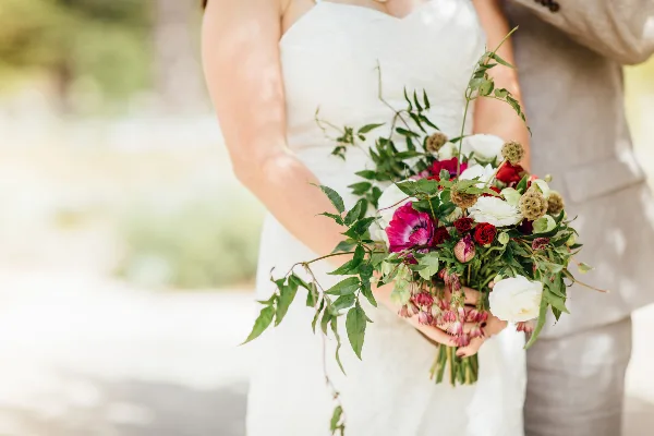 A bride in a white dress holding a large, custom wedding bouquet featuring red and white flowers and greenery.