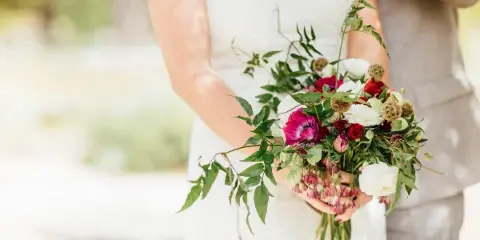 A bride in a white dress holding a large, custom wedding bouquet featuring red and white flowers and greenery.