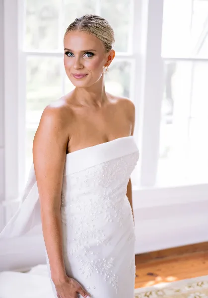 A bride with styled hair and professional makeup wearing a white wedding dress.