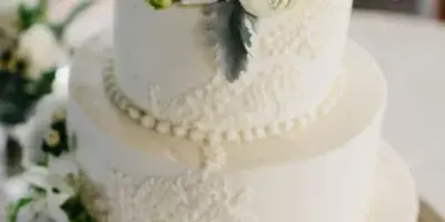 A three-tiered white wedding cake with piped lace details and a floral arrangement on top.