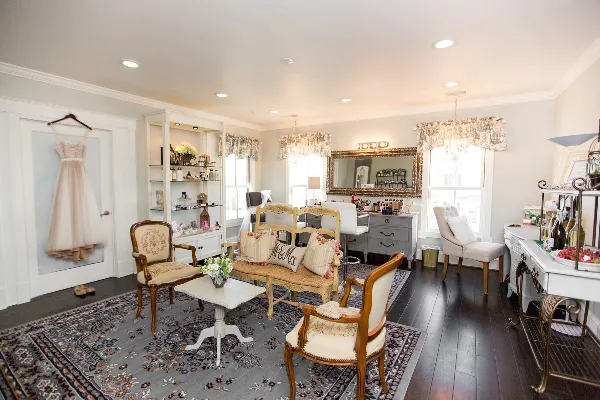 Interior view of a bridal makeup studio featuring a vanity station, a hanging wedding dress, and a seating area with a 'Mr & Miss' pillow.
