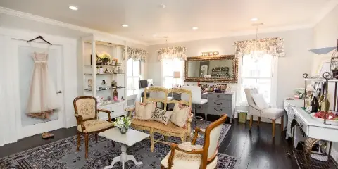 Interior view of a bridal makeup studio featuring a vanity station, a hanging wedding dress, and a seating area with a 'Mr & Miss' pillow.