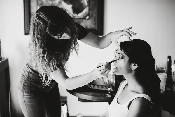 A makeup artist applying eye makeup to a seated client.
