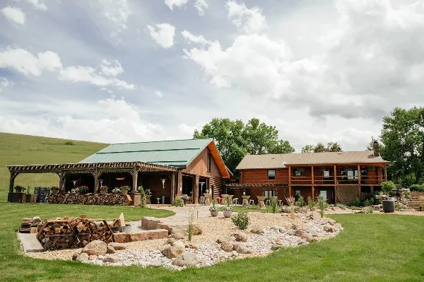 Exterior view of the Big Vista Ranch main lodge and patio area featuring log construction, a green metal roof, and outdoor seating.