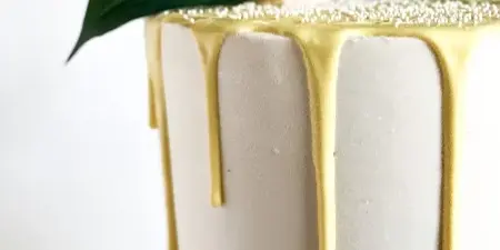 A white frosted cake with yellow drip glaze topped with lemon slices and green leaves.