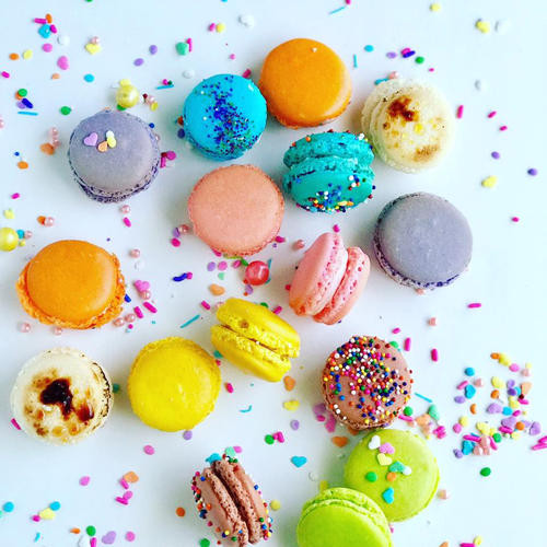 An assortment of colorful macarons and sprinkles on a white surface.