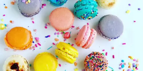 An assortment of colorful macarons and sprinkles on a white surface.