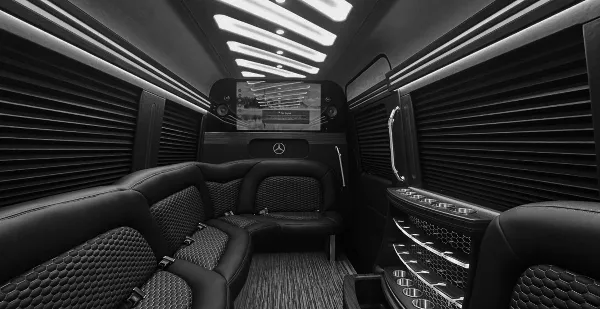 Interior view of a luxury party bus featuring black leather seating, ambient lighting, and a Mercedes-Benz logo.