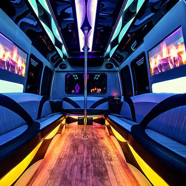Interior view of a party bus with blue and yellow LED lighting, leather bench seating, a central dance pole, and flat screen televisions.