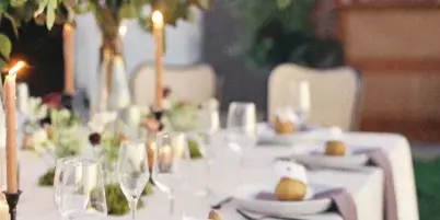 A professionally designed wedding table setting featuring a white tablecloth, tall floral arrangement, taper candles, and place settings with napkins.