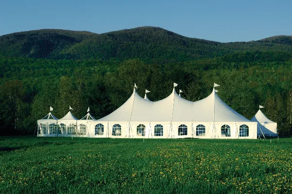 A large white event tent with multiple peaks set up in a grassy field with mountains in the background.
