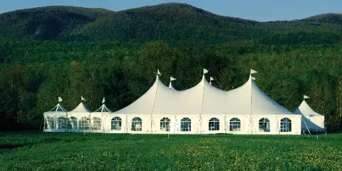 A large white event tent with multiple peaks set up in a grassy field with mountains in the background.