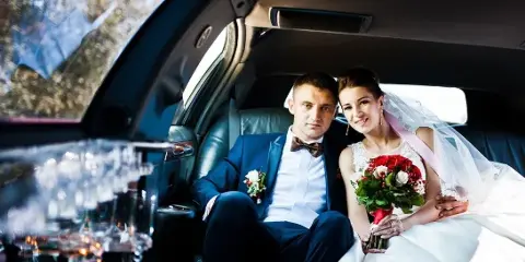 A bride and groom sitting in the back seat of a luxury car.