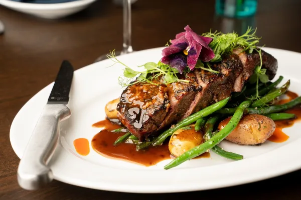A plated steak dish with green beans, potatoes, and a flower garnish on a white plate.