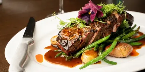 A plated steak dish with green beans, potatoes, and a flower garnish on a white plate.