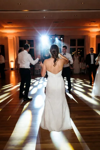 Bride and groom dancing on a wooden dance floor under bright event lighting during a wedding reception.