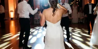 Bride and groom dancing on a wooden dance floor under bright event lighting during a wedding reception.