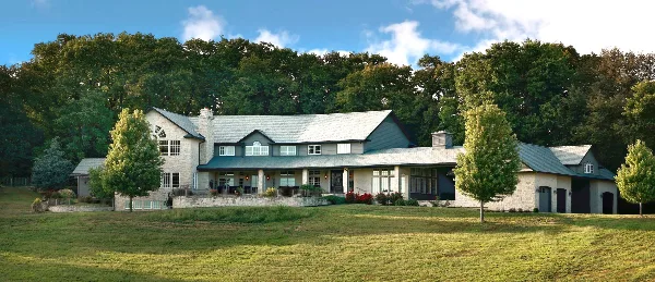 Exterior view of a large stone and wood country estate with manicured lawns and trees.