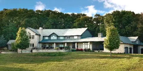Exterior view of a large stone and wood country estate with manicured lawns and trees.