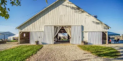 White barn wedding venue with open doors, event setup inside, and surrounding farm property.